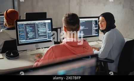 Giovani studenti intelligenti che studiano all'università con diversi compagni di classe multietnici. Gli studiosi collaborano in College Room su computer Science Project, scrivendo software Code in Successful Teamwork. Foto Stock