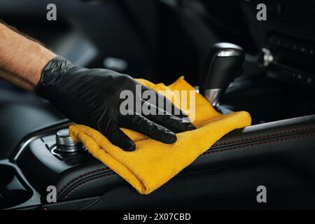pulizia degli interni dell'auto. primo piano della mano con un panno in microfibra sulla console centrale Foto Stock