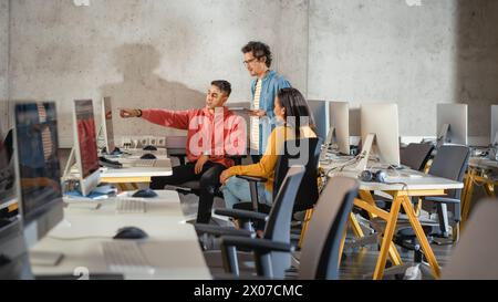 Gruppo eterogeneo di studenti di sesso femminile e maschile seduti insieme nella sala infografica, che collaborano a un progetto universitario. Giovani studiosi che parlano, studiano lo sviluppo di software o l'informatica. Foto Stock