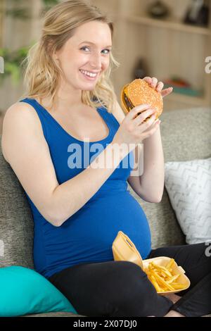 una donna incinta con la pancia si gode un hamburger Foto Stock