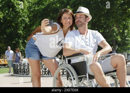 donna che fa un selfie con il marito paralizzato in città Foto Stock