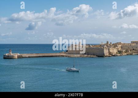 Una barca entra nella baia di la Valletta passando vicino alla Ricasoli East Breakwater, Kalkara, Malta Foto Stock