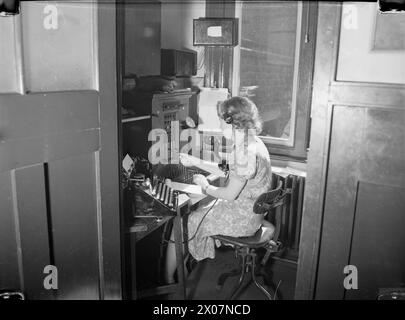 PERSONE AL LAVORO IN TEMPO DI GUERRA: VITA DI TUTTI I GIORNI IN TEMPO DI GUERRA IN GRAN BRETAGNA, 1940 - Una donna operatrice di centralino al lavoro su un piccolo centralino per uffici, da qualche parte in Gran Bretagna, 1940. L'apparecchiatura utilizzata in questo lavoro include una cuffia per telefono e un quadrante, un tubo di comunicazione legato al collo e una macchina da scrivere Foto Stock