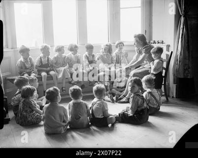 AMERICAN AID TO BRITAIN: LIFE AT SYSTON COURT NURSERY, THE SARA DELANO ROOSEVELT HOME, GLOUCESTERSHIRE, INGHILTERRA, 1942 - i bambini siedono in cerchio, alcuni sul pavimento e altri sul sedile accanto alla finestra, per ascoltare una storia raccontata al Syston Court Nursery nel Gloucestershire Foto Stock