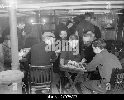 UOMINI IN FUGA DELLA ROYAL NAVY. SETTEMBRE 1941, A BORDO DI DRIFTERS A SCAPA. MIGLIAIA DI PESCATORI IN TEMPO DI PACE LAVORANO COME UOMINI IN FUGA CON LA ROYAL NAVY. L'INTERO TRASPORTO DEL PERSONALE, DELL'APPROVVIGIONAMENTO ALIMENTARE E DELLA POSTA ALLE NAVI DA GUERRA ALL'ANCORA VIENE EFFETTUATO DAGLI UOMINI DRIFTER. SERVONO ANCHE STAZIONI STRANIERE DOVE LE UNITÀ DELL'ESERCITO E DELL'AERONAUTICA MILITARE SONO DI STANZA A MIGLIA DI DISTANZA DA QUALSIASI LUOGO. A SCAPA C'ERANO QUASI 200 DRIFTER SUI LIBRI E OLTRE 1000 UOMINI. - Un'altra partita nella cabina della nave della missione Drifter, un mazzo di pesca convertito dove gli uomini della deriva si riuniscono la sera. Due di Foto Stock