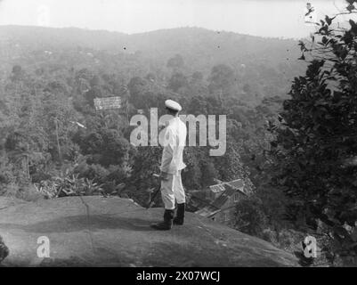 SOTTUFFICIALE PALENTHORPE A LEICESTER, UN PICCOLO VILLAGGIO VICINO FREETOWN, SIERRA LEONE. - Il sottufficiale Palenthorpe guarda in basso il villaggio di Leicester. La Naval Rest Home si erge in alto sul lato della montagna sopra il villaggio. Titolo originale della seconda guerra mondiale e didascalia con questa fotografia: MARINAIO CHE È DIVENTATO IL VILLAGGIO AFRICANO SQUIRE. GINGER-HAIRED PETTY OFFICER PALENTHORPE È LO "SCUDIERO" DI LEICESTER, IL PICCOLO VILLAGGIO AFRICANO VICINO FREETOWN, SIERRA LEONE. DOPO 18 MESI DI CONSIGLI AMICHEVOLI AI NATIVI, C'È ORA UNA COMPLETA FIDUCIA RECIPROCA E COMPRENSIONE TRA LORO E 'MISTER GINGER Foto Stock