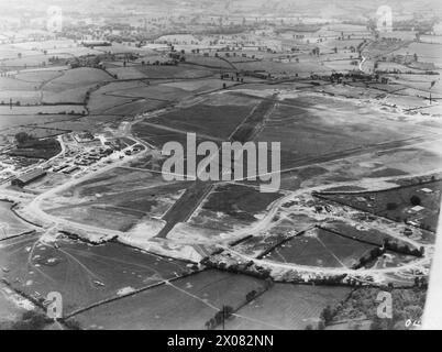 ROYAL AIR FORCE FIGHTER COMMAND, 1939-1945. - Vista aerea obliqua dell'aeroporto di Exeter, Devon, da nord-est. I danni causati dai gravi raid aerei notturni montati contro l'aeroporto nell'aprile e nel maggio 1941 sono ancora evidenti tra gli edifici del sito tecnico sulla sinistra, compreso il grande hangar civile pre-bellico utilizzato dalla Royal Aircraft Establishment. In primo piano sono state eseguite riparazioni sulle superfici erbose riempiendo crateri bomba con macerie provenienti da case bombardate a Exeter. Gli aerei, molti dei quali appartengono alla Gunnery Research Unit, sono dispersi intorno all'aerofiel Foto Stock