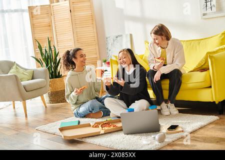 Un gruppo variegato di ragazze adolescenti sedute sul pavimento, gustando la pizza insieme in un ambiente accogliente. Foto Stock