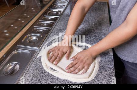 Lo chef prepara le mani di impasto per pizza. L'impasto per la pizza viene arrotolato e impastato. Cuocere le mani impastando l'impasto e spolverando un pezzo di impasto con farina di grano bianco Foto Stock