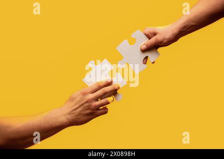 Uomini che tengono e mettono insieme un pezzo di puzzle. Due mani che cercano di collegare un pezzo del puzzle su sfondo grigio. Primo piano mano di Foto Stock