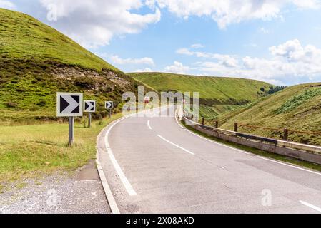 La Chevron Road segnala una curva stretta lungo una tortuosa strada di passo di montagna in Inghilterra in una giornata estiva parzialmente nuvolosa Foto Stock