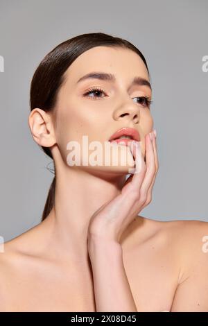 Una giovane donna con i capelli bruna posa graziosamente con la mano delicatamente appoggiata sul viso in un ambiente da studio. Foto Stock