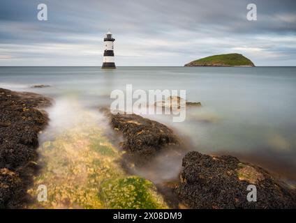 Il faro di Trwyn Du a Penmon Point in Anglesey è circondato da una marea crescente in un pomeriggio coperto mentre le nuvole scorrono nel cielo sopra. Foto Stock