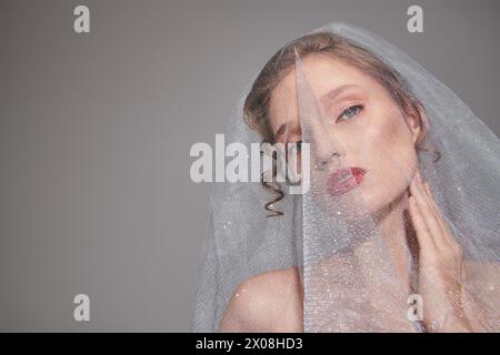 Una giovane donna posa in uno studio, indossando un velo sulla testa, trasuda bellezza ed eleganza classiche. Foto Stock