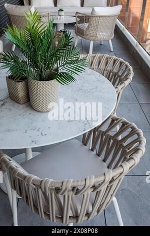 Un elegante patio esterno con tavolo in marmo bianco, sedie intrecciate e lussureggianti piante in vaso, che riflettono un ambiente contemporaneo e accogliente Foto Stock
