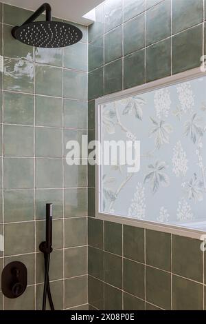 Un bagno dal design elegante con piastrelle verdi quadrate e grande soffione doccia a pioggia, completato da una finestra a motivi floreali Foto Stock