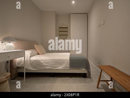 Un accogliente e moderno interno minimalista con un letto bianco, una lampada elegante, tonalità neutre e un'atmosfera calda e luminosa Foto Stock