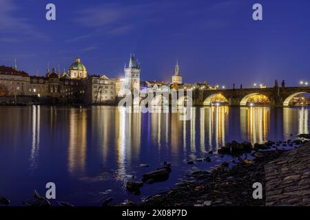 Una tranquilla scena crepuscolare che cattura il Ponte Carlo illuminato che si riflette sul fiume Moldava a Praga, con edifici storici sullo sfondo Foto Stock