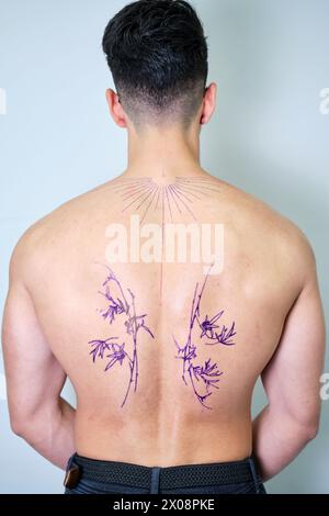 Una vista posteriore di un uomo irriconoscibile, con profili preliminari del tatuaggio, che anticipa l'intricato lavoro di inchiostro in uno studio professionale Foto Stock