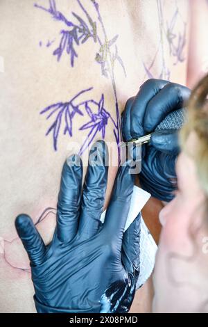 Vista ravvicinata di una donna irriconoscibile che tatua un disegno sulla pelle di un cliente in uno studio di tatuaggio pulito. Foto Stock
