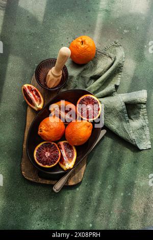 Natura morta con agrumi con arance di sangue intere e dimezzate in un ambiente rustico con una centrifuga Foto Stock