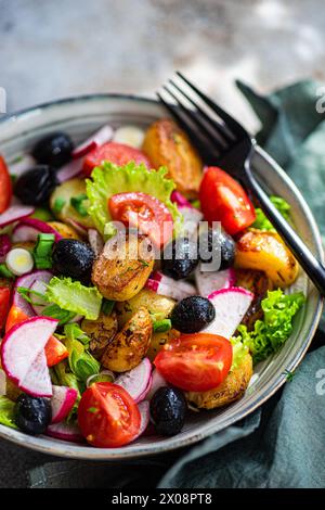 Una vivace ciotola di insalata mediterranea, con patate arrosto, olive soffici, pomodori ciliegini, cipolle primaverili croccanti, lattuga e ravanelli a fette, e. Foto Stock