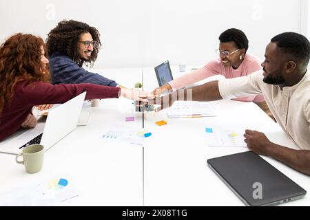 Team diversificato di professionisti che celebrano il successo con un pugno di sbalzo su una scrivania, collaborando in un ambiente di ufficio luminoso. Foto Stock