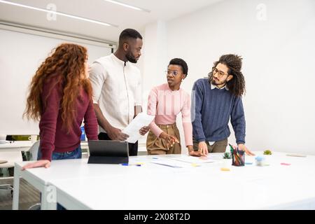 Team eterogenei che collaborano in un ambiente di ufficio moderno, con uomini e donne di diverse origini etniche, impegnati in conversazioni su documenti cartacei Foto Stock