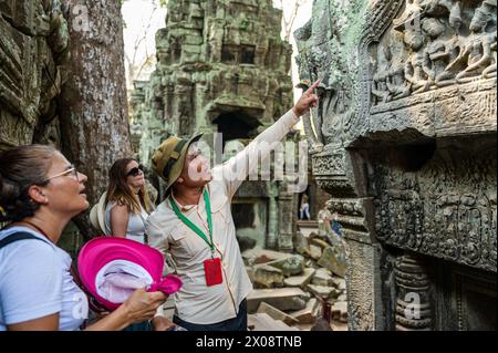 Una guida turistica maschile esperta ti indicherà con passione le dettagliate incisioni alle donne turistiche del tempio di Angkor Wat, tra antiche rovine. Foto Stock