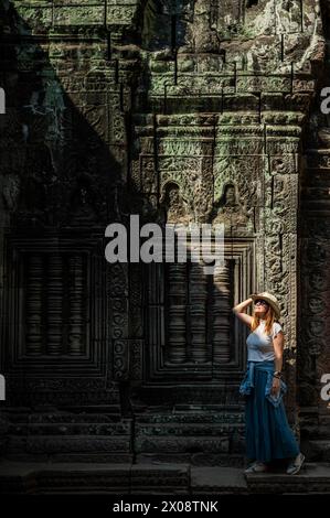 Una donna turistica ammira le intricate incisioni sulle pareti dello storico tempio di Angkor Wat a Siem Reap, in Cambogia, evidenziate dalla luce del sole. Foto Stock