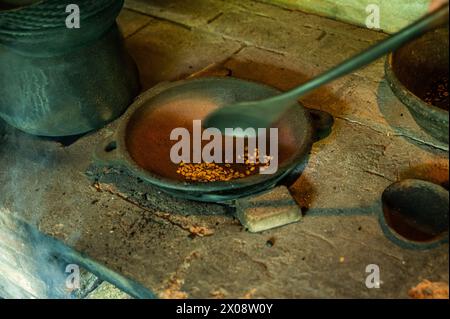 Un primo piano di chicchi di caffè appena tostati in una tradizionale pentola di argilla sopra una stufa a legna, catturando l'essenza dell'autentico caffè balinese. Foto Stock