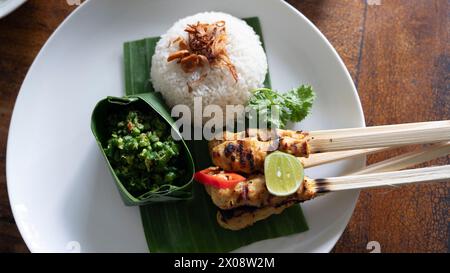 Un tradizionale pasto balinese con satay di pollo su spiedini, servito con riso al vapore condito con scalogno fritto, un lato di sambal di peperoncino verde, e. Foto Stock