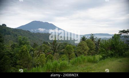 Un tranquillo paesaggio caratterizzato dall'iconico Monte Agung di Bali che torreggia sulla fitta vegetazione tropicale, con nuvole che poggiano dolcemente sul suo pendio Foto Stock