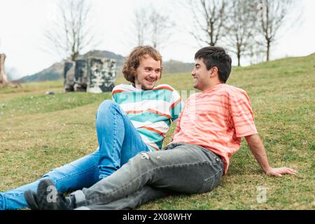Due uomini, una coppia transessuale amorevole, condividono una risata mentre si rilassano sull'erba, godendosi un momento spensierato e intimo insieme Foto Stock