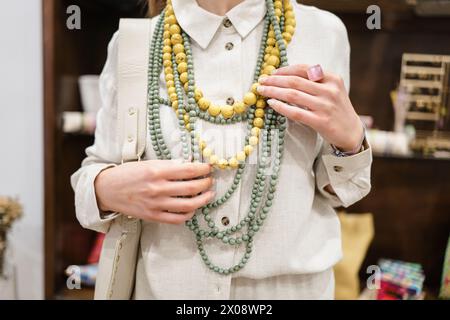 Donna elegante con collane con perline a strati in tonalità primaverili, che toccano con eleganza gli accessori con mani curate Foto Stock