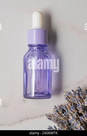 Dall'alto bottiglia contagocce in vetro viola per olio essenziale accanto a un mazzo di fiori secchi di lavanda su uno sfondo di pietra, raffiguranti cosmetici naturali Foto Stock