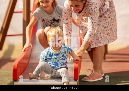La famiglia con un bambino affetto da sindrome di Down si diverte a divertirsi sulle attrezzature per il parco giochi. Foto Stock