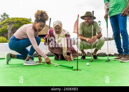 Gruppi diversi di amici che si divertono insieme a una partita di minigolf in una giornata di sole. Foto Stock