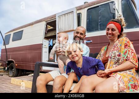 Da sotto una famiglia di quattro persone si gode il ponte autocostruito accanto alla casa del furgone, mostrando il loro stile di vita unico. Foto Stock
