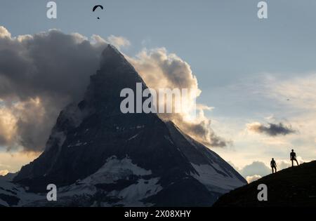 Il Cervino incombe sugli escursionisti e su un parapendio in questa serena scena di avventura alpina al tramonto, che mostra la grandezza della natura Foto Stock