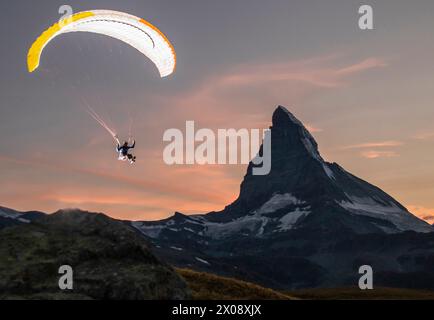 Un parapendio si libra sullo sfondo di un tramonto panoramico con la maestosa montagna del Cervino che torreggia in lontananza Foto Stock