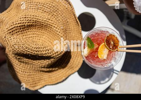 Vista dall'alto di una bevanda rinfrescante guarnita con limone a parte un cappello di paglia in un luminoso giorno d'estate. Foto Stock