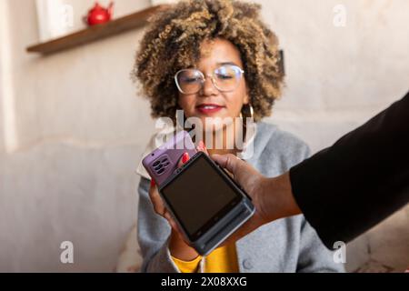 Una donna sorridente con capelli ricci che paga tramite telefono cellulare, trasmette connettività e vita moderna Foto Stock