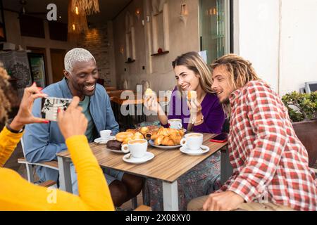 Un gruppo eterogeneo di amici condivide le risate e gusta pasticcini e caffè insieme in un accogliente caffè, catturando un momento di gioia Foto Stock
