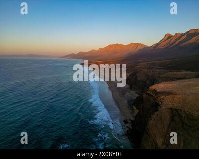 Tramonto tranquillo sulla tranquilla spiaggia di Cofete a Fuerteventura, che mostra lo splendido contrasto tra le aspre montagne e il mare calmo Foto Stock