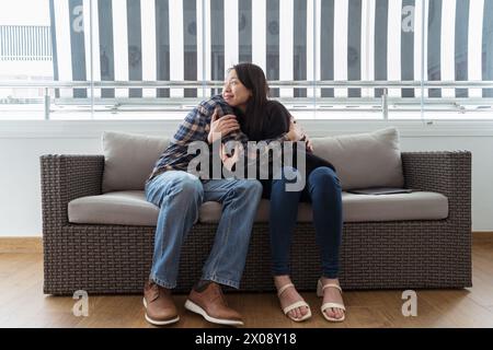 Una donna asiatica e un uomo caucasico si abbracciano su un divano mostrando amore e compagno in tutte le culture Foto Stock