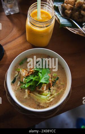 Accogliente ciotola di zuppa cremosa guarnita con erbe aromatiche, abbinata a un rinfrescante frullato di mango Foto Stock