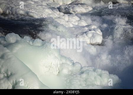 Primo piano di un fiume ghiacciato con intricate formazioni di ghiaccio e un'acqua che scorre rapidamente in Islanda, che mostra la dura bellezza della stagione invernale Foto Stock