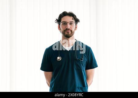 Un operatore medico maschile concentrato in scrub con uno stetoscopio è pronto a fornire assistenza esperta Foto Stock