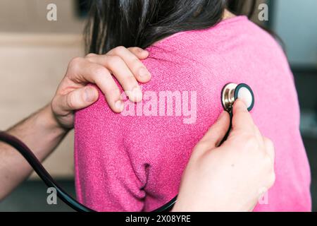 Vista a spalla di un medico anonimo che utilizza uno stetoscopio sulla schiena del paziente, ascoltando i chiari suoni polmonari in un esame medico Foto Stock